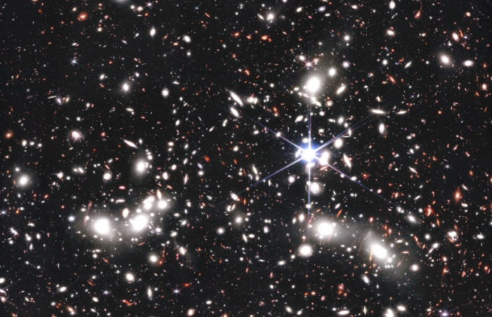 This JWST color image shows clusters galaxies in bright wight, while distant background galaxies are red and often distorted by the gravitational lensing effect.
